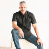 Editor Two Pocket Short Sleeve Men's Utility Shirt In Pure Black Mercerized Cotton On Body Sitting Image
